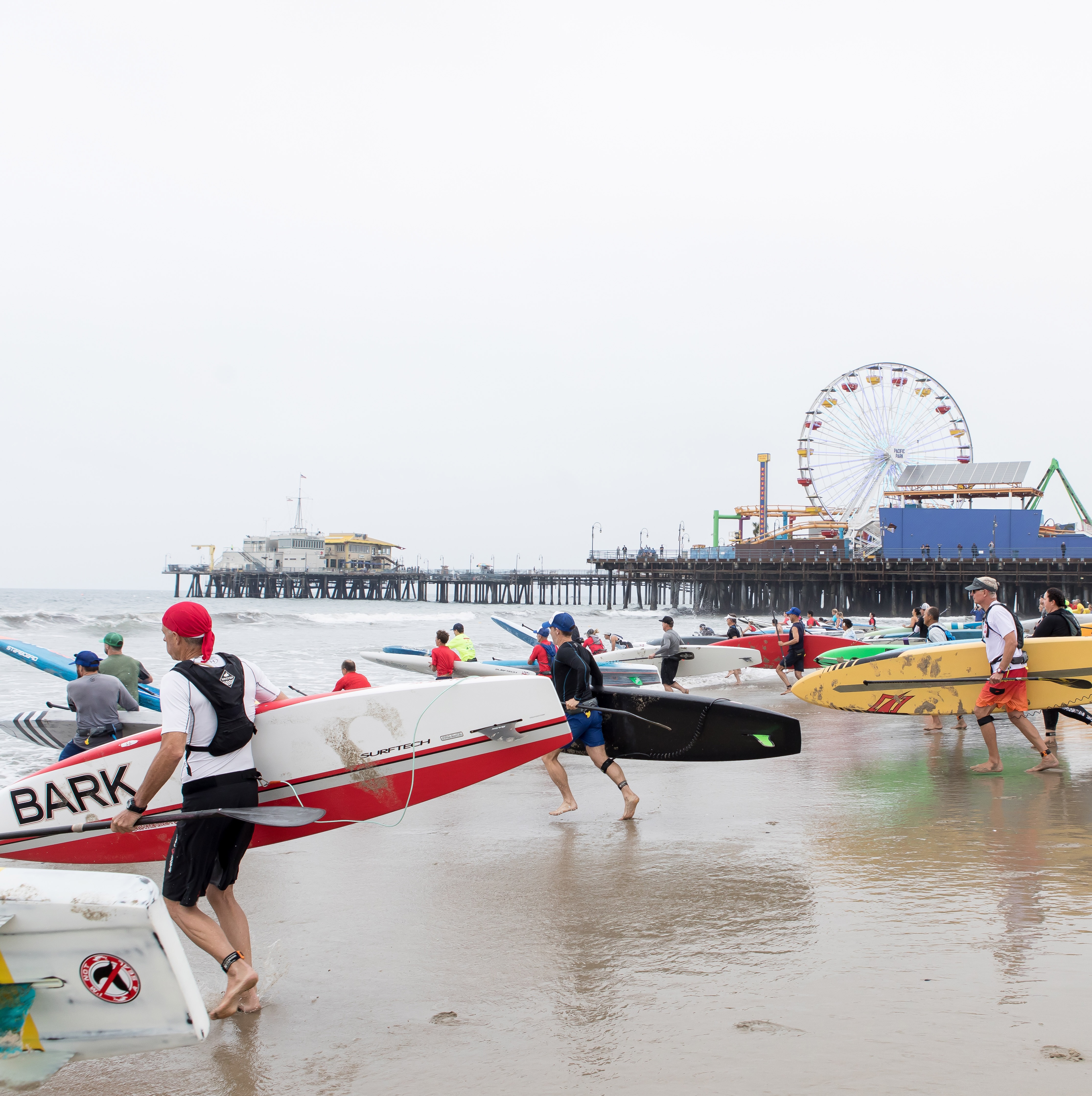 Surfers running into the Pacific Ocean with the Santa Monica Pier behind them in California