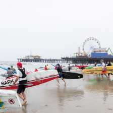 Surfers running into the Pacific Ocean with the Santa Monica Pier behind them in California